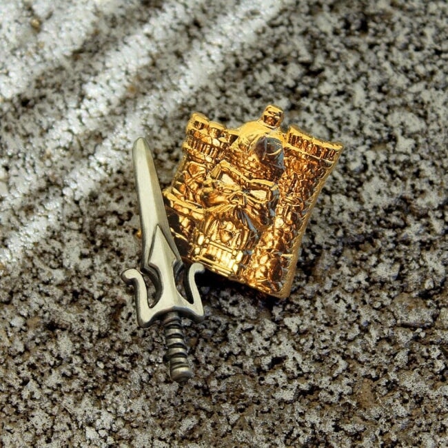 shot of the 3D gold castle grayskull and power sword pin on a gravel and rock surface