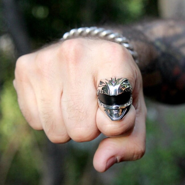 shot of the green ranger ring on the pointer finger of a man with a fist with plants in the back