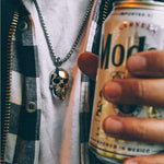 shot of a man wearing the 2 tone skull pendant from the han cholo skulls collection holding a modelo