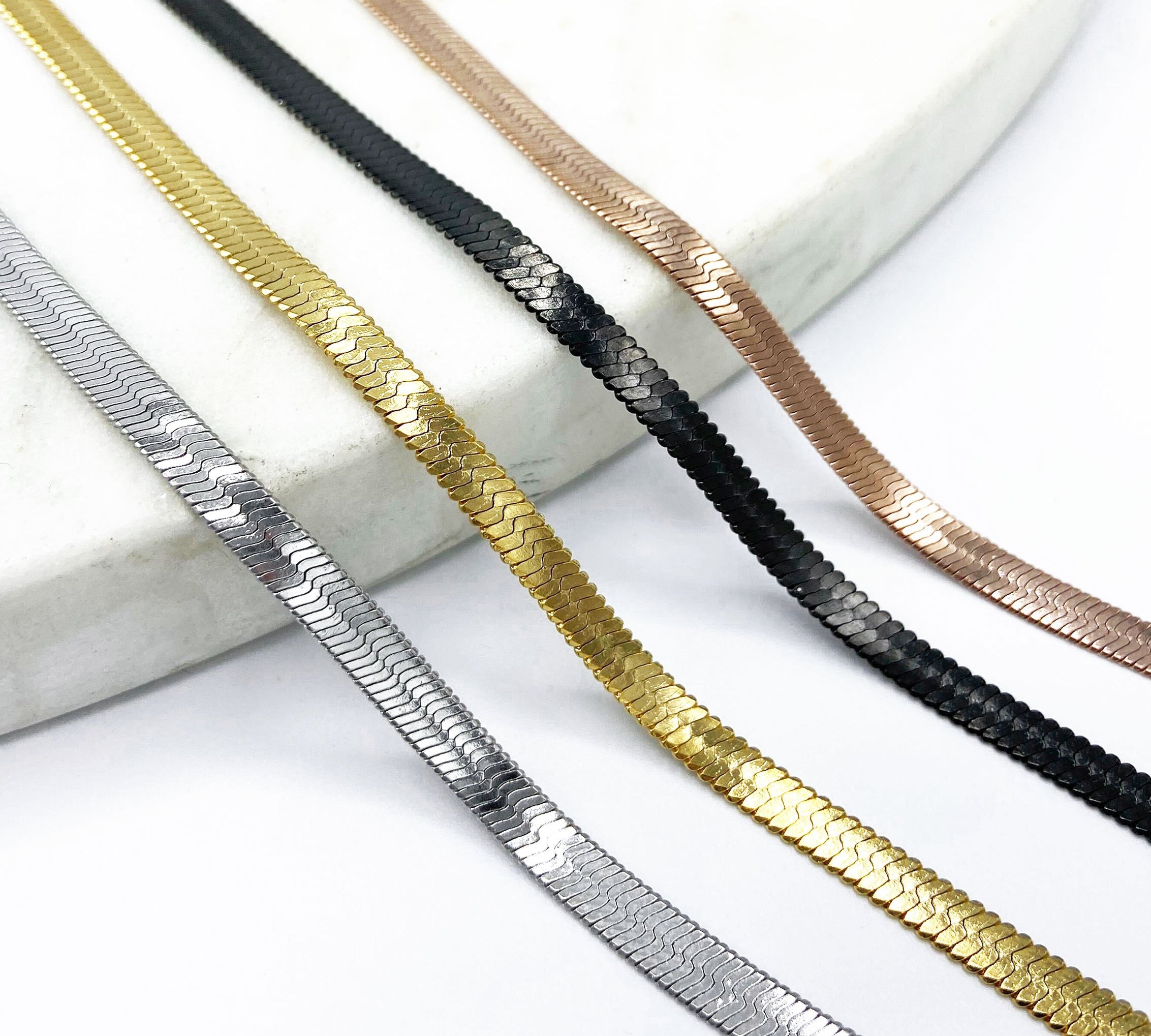 shot of the of the gunmetal, silver, gold and rose gold herring bone chains side by side on marble