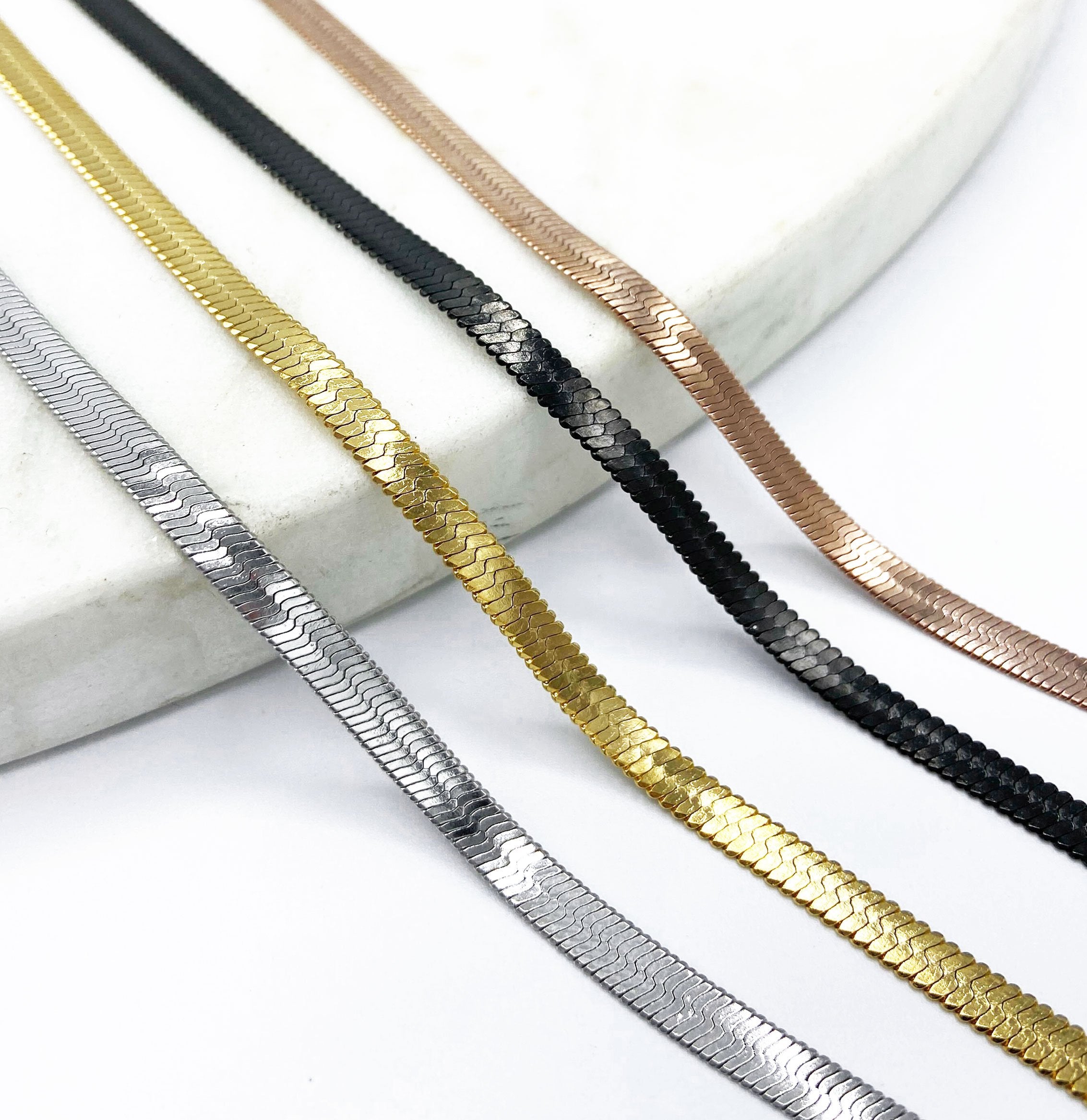 shot of the of the gunmetal, silver, gold and rose gold herring bone chains side by side on marble