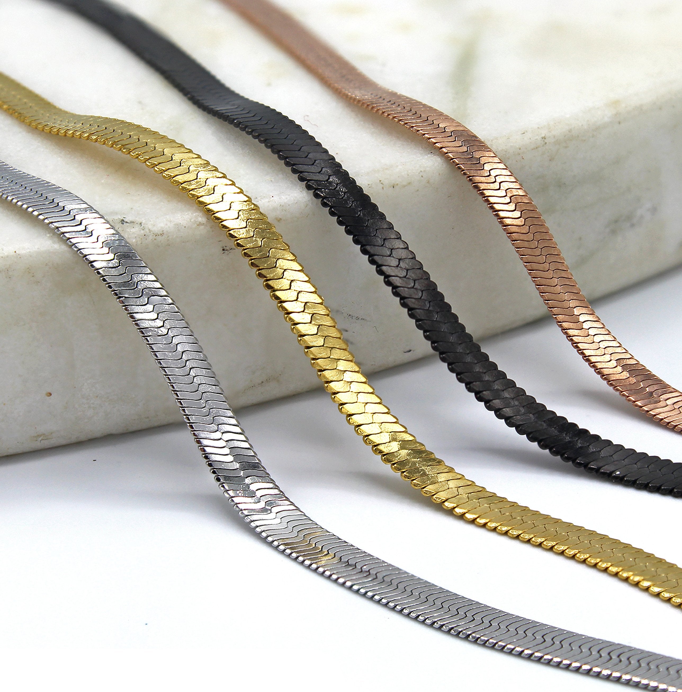 shot of the of the gunmetal, silver, gold and rose gold herring bone chains side by side on marble