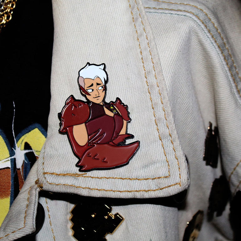 shot of the scorpia enamel pin on a grey jean jacket collar with other pins on the jacket