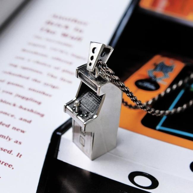 shot of the arcade pendant in silver on a page of a book showing a classic arcade machine
