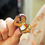 picture of archer bow enamel pin being held by someone with their fingers on a blurred background
