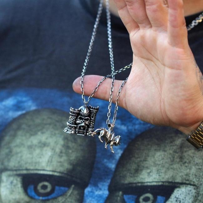 shot of a man holding up the castle grayskull and battlecat pendant in wearing a pink floyd tshirt