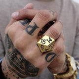 shot of a man with tattoos and a tan shirt wearing a gold watch and the gold D20 ring