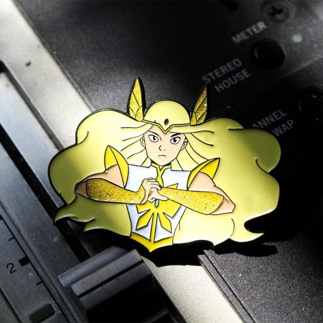 shot of she-ra enamel pin for the honor of grayskull in shadow with light shining on the pin