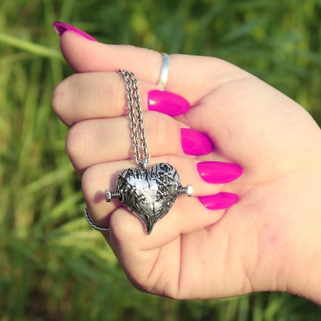shot of a woman wearing pink nail polish holding the silver frankenheart pendant in her hand