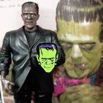 shot of a frankenstein toy holding the frankenstein pin with a frankenstein illustration behind it