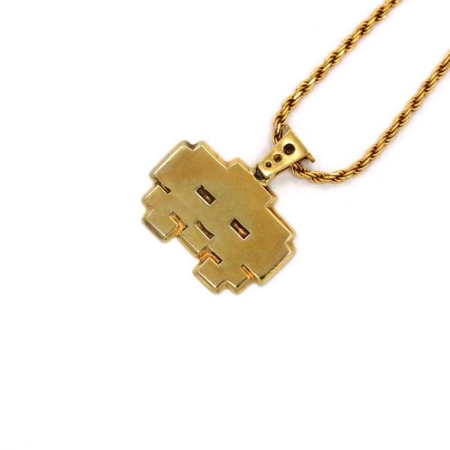 right angle view of the grumpy invader pendant in gold on a white background