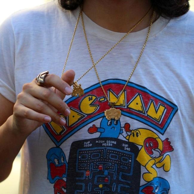 shot of a man wearing a vintage pac man t shirt holding up the grumpy invader pendant in gold