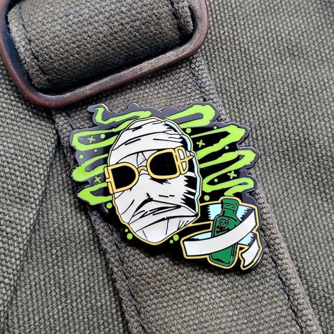 shot of the invisible man enamel pin on a army green backpack strap