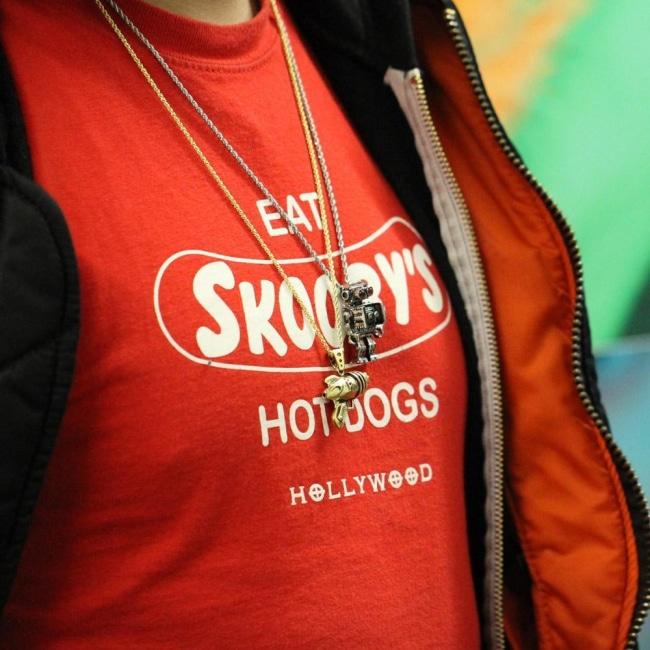 shot of a man in a red graphic t shirt wearing the robot pendant and the ray gun pendant in gold