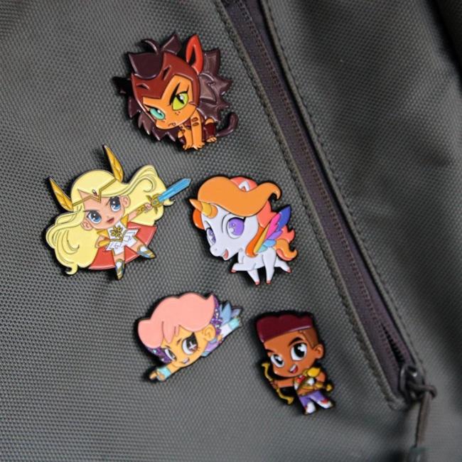 picture of all 5 she-ra chibi enamel pins pinned to a backpack right next to a zipper