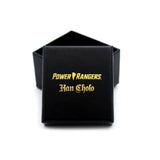 shot of the mighty morphin power rangers black a gold foil ring box on a white surface